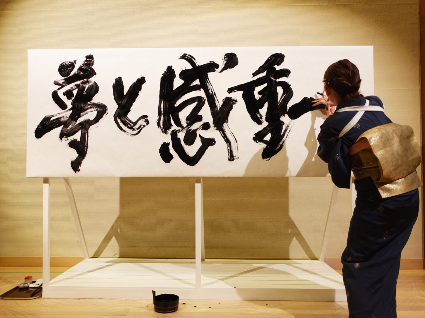 書家・根本みきが「DIグループ安全衛生協議会 創立20周年記念祝賀会」で、DIグループ代表・小板橋社長のモットー「夢と感動」を力強く揮毫する書道パフォーマンスを披露。参加者の夢が実り、感動が広がるよう願いを込めた作品。