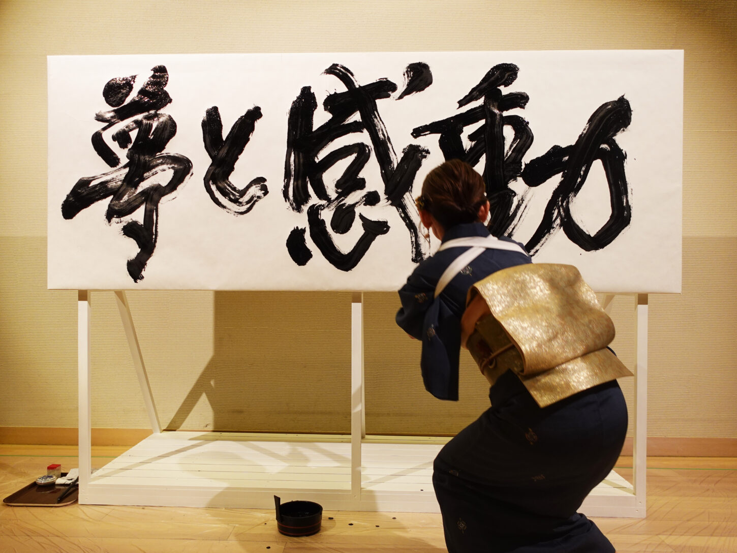 書家・根本みきが「DIグループ安全衛生協議会 創立20周年記念祝賀会」で、DIグループ代表・小板橋社長のモットー「夢と感動」を力強く揮毫する書道パフォーマンスを披露。参加者の夢が実り、感動が広がるよう願いを込めた作品。