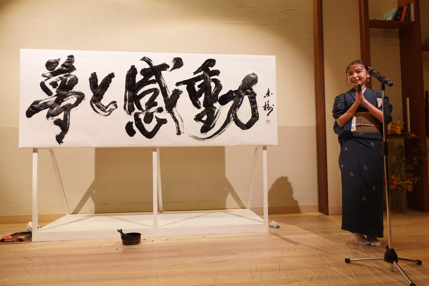 書家・根本みきが「DIグループ安全衛生協議会 創立20周年記念祝賀会」で、DIグループ代表・小板橋社長のモットー「夢と感動」を力強く揮毫する書道パフォーマンスを披露。参加者の夢が実り、感動が広がるよう願いを込めた作品。