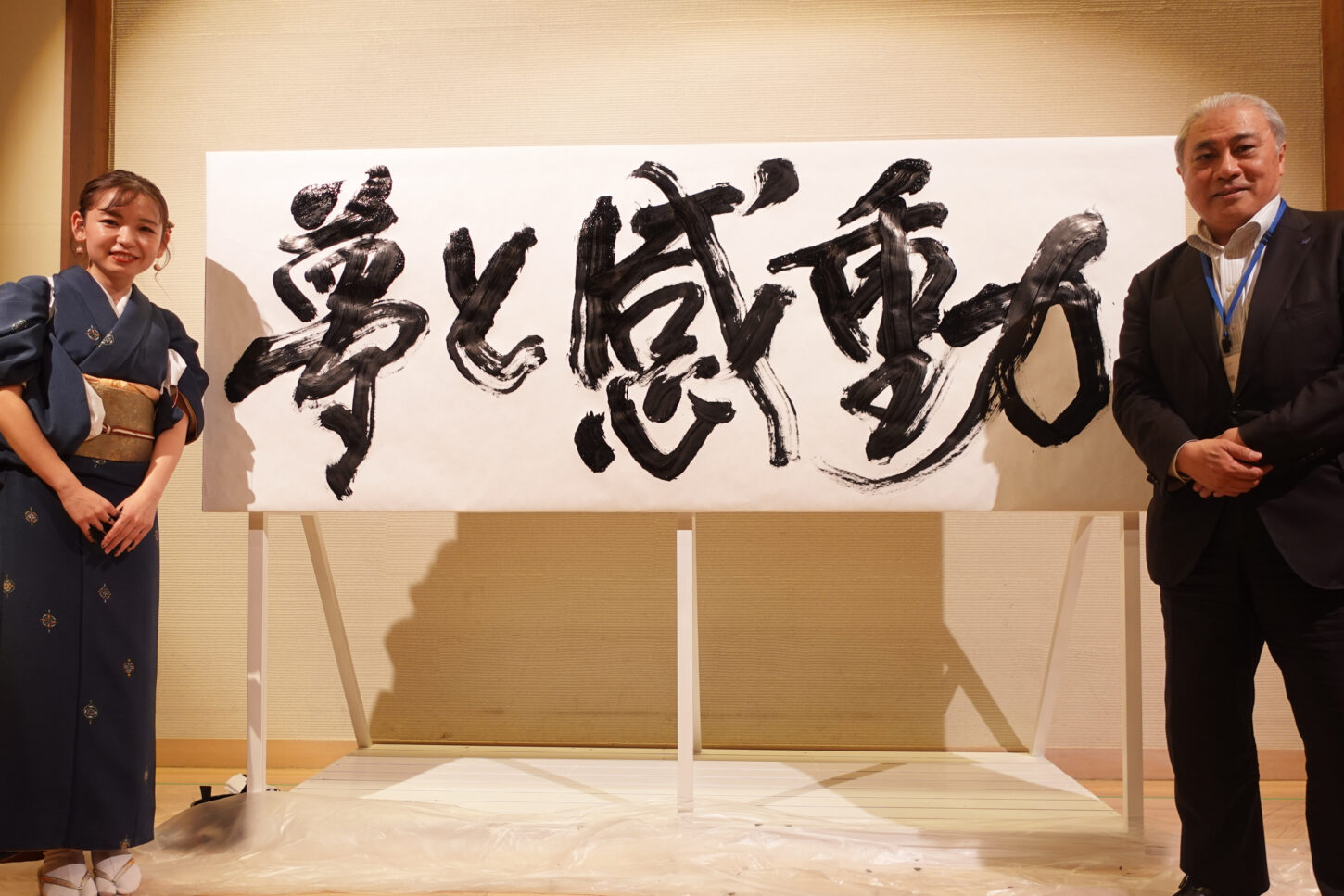 書家・根本みきが「DIグループ安全衛生協議会 創立20周年記念祝賀会」で、DIグループ代表・小板橋社長のモットー「夢と感動」を力強く揮毫する書道パフォーマンスを披露。参加者の夢が実り、感動が広がるよう願いを込めた作品。