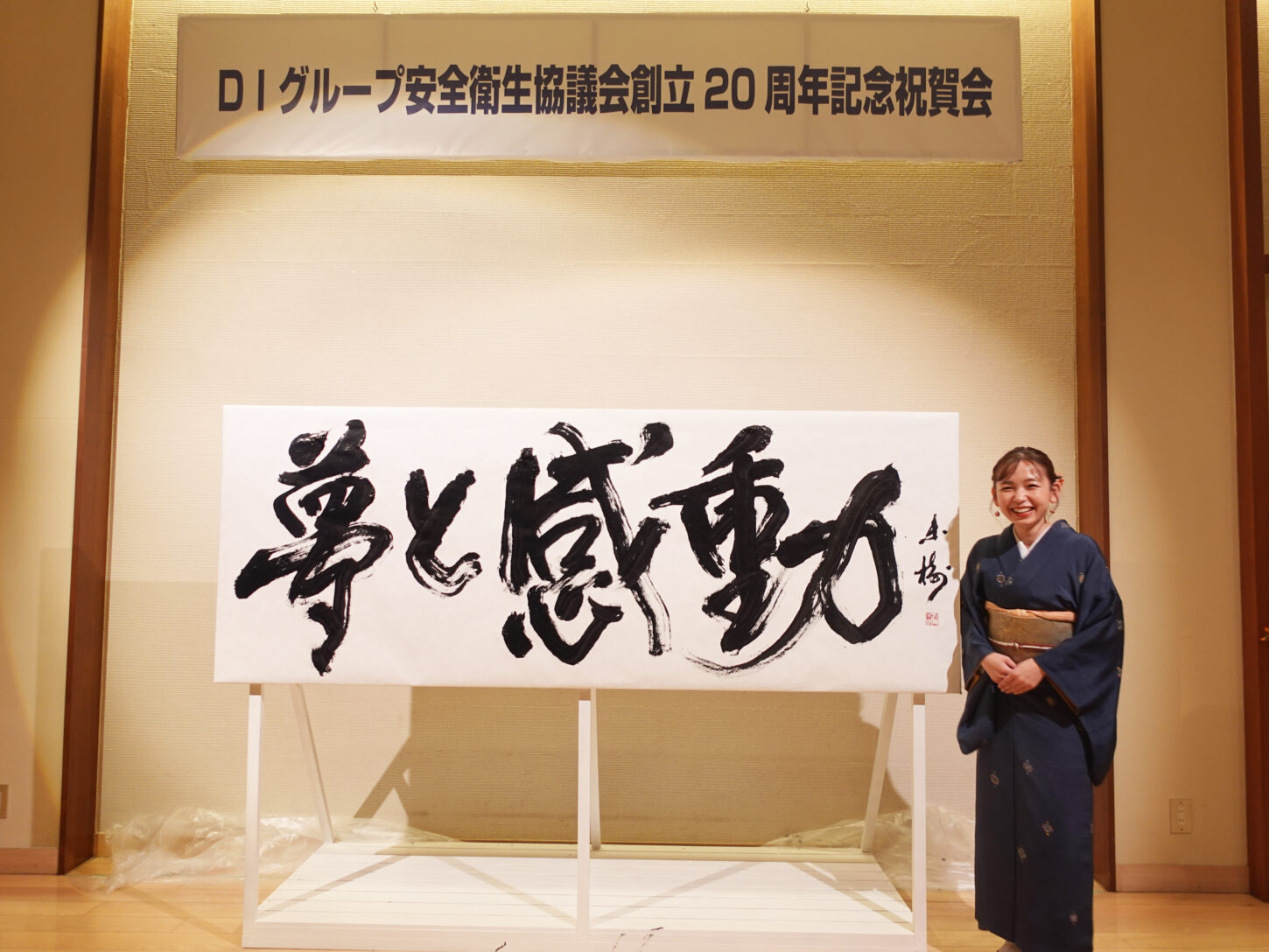 書家・根本みきが「DIグループ安全衛生協議会 創立20周年記念祝賀会」で、DIグループ代表・小板橋社長のモットー「夢と感動」を力強く揮毫する書道パフォーマンスを披露。参加者の夢が実り、感動が広がるよう願いを込めた作品。