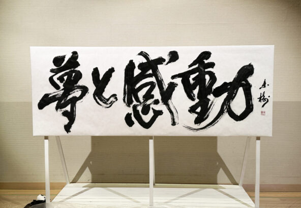 書家・根本みきが「DIグループ安全衛生協議会 創立20周年記念祝賀会」で、DIグループ代表・小板橋社長のモットー「夢と感動」を力強く揮毫する書道パフォーマンスを披露。参加者の夢が実り、感動が広がるよう願いを込めた作品。