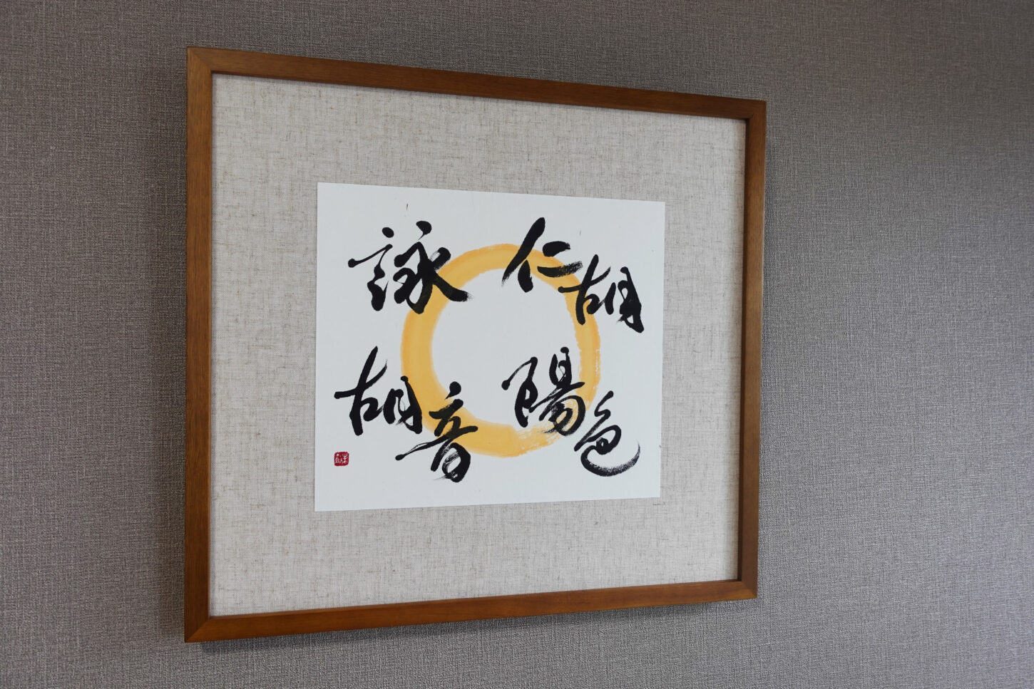 木目調フレームに額装された、書家・根本みきによるアート書道作品。黄金色の円相の上に、お子様４名の名を柔らかくつなぐように書き上げ、家族の温かなつながりと印象を表現した一作。