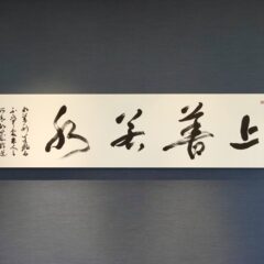 上善若水|株式会社東栄住宅ご依頼の書道作品。老子の言葉をテーマに、水の流れを想起させる筆致で揮毫。社長室の空間と調和するパネル表装で仕上げた、書家・根本みきによる企業向けオーダーメイド書作品。