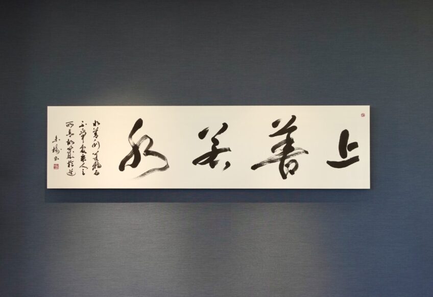上善若水｜株式会社東栄住宅ご依頼の書道作品。老子の言葉をテーマに、水の流れを想起させる筆致で揮毫。社長室の空間と調和するパネル表装で仕上げた、書家・根本みきによる企業向けオーダーメイド書作品。